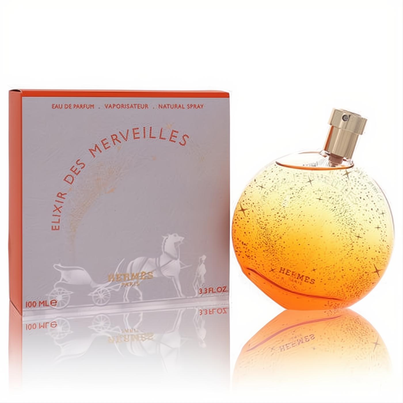 Hermes Elixir Des Merveilles 3.3 oz Eau De Parfum. Radiant amber spherical bottle with gold cap & starry design, beside its elegant white box.