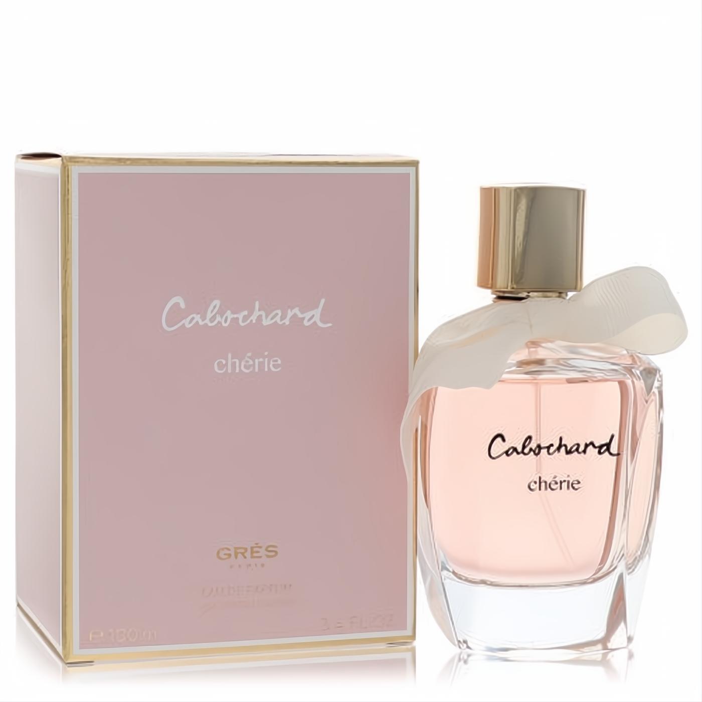 Cabochard Cherie 3.4 oz EDP: Elegant clear glass bottle with soft pink liquid, gold cap, and delicate cream ribbon, beside its chic pink and gold box.