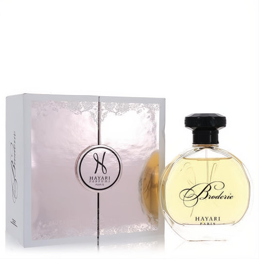 Hayari Broderie women's EDP in a clear round bottle with a black cap, beside its luxurious white and silver lace-patterned box.
