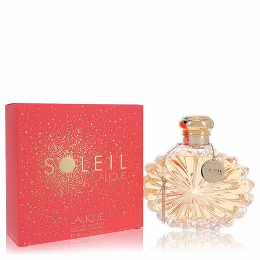 Lalique Soleil 3.3 oz EDP. Luxurious sunburst glass bottle with gold cap and charm, next to its sparkling coral red box.