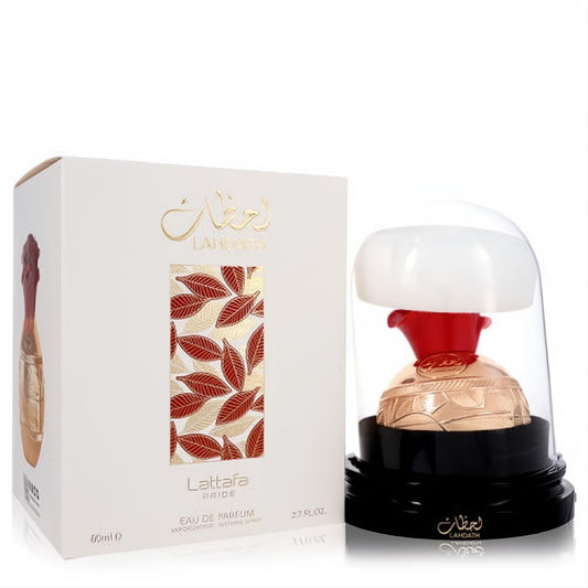 Luxurious Lattafa Pride Lahdath 2.7 oz unisex EDP. Gold bottle with red top under glass dome, beside a white box with elegant red leaf design.