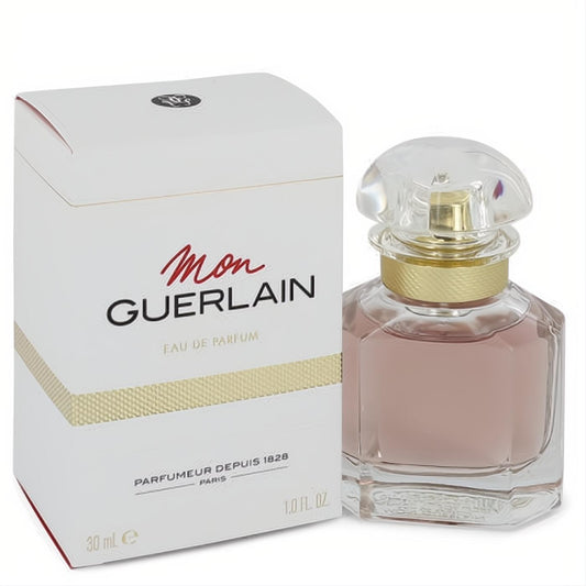 Mon Guerlain 1 oz Eau De Parfum. Elegant faceted glass bottle with light pink liquid, gold collar, and clear cap, beside its white and gold box.