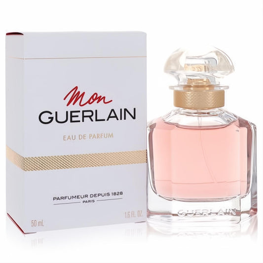 Luxurious Mon Guerlain Eau De Parfum 1.6 oz spray in an elegant clear glass bottle with pink fragrance, gold neck, and iconic quadrilobe stopper, beside its white branded box.