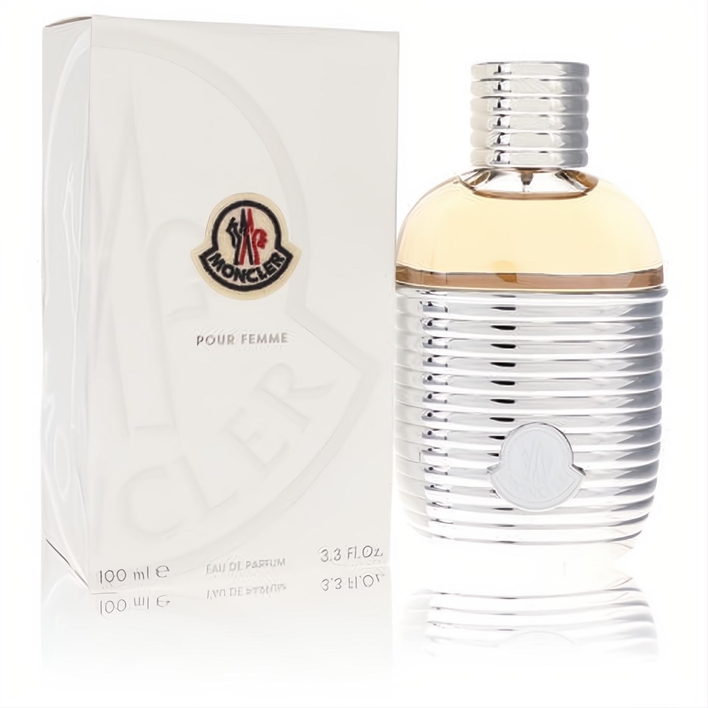 Luxurious Moncler Pour Femme Eau De Parfum, 100ml. Sleek silver ribbed bottle with warm amber liquid and iconic logo, beside its crisp white box.