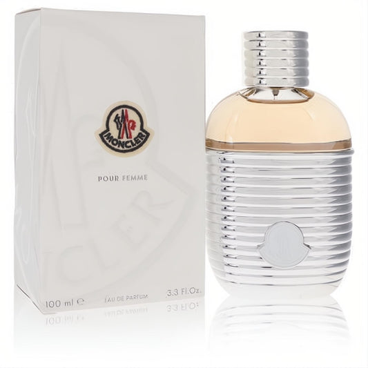 Moncler Pour Femme EDP 3.3 oz. Luxurious silver ribbed bottle, clear glass with amber liquid, and iconic Moncler logo.