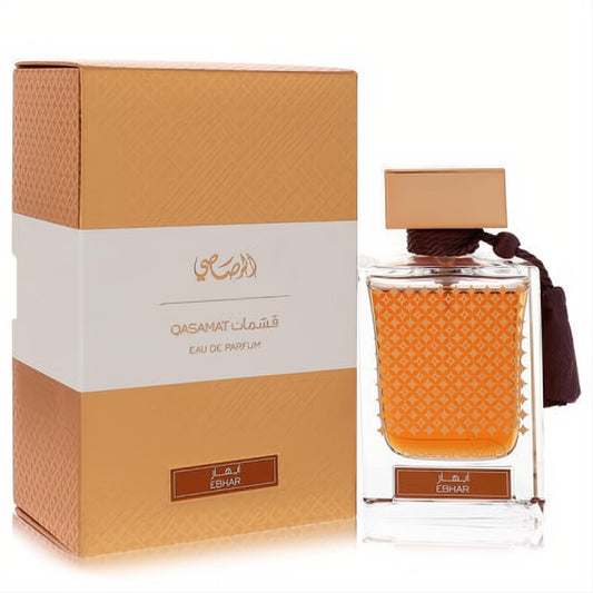 Rasasi Qasamat Ebhar unisex Eau De Parfum. Elegant amber liquid in a patterned glass bottle with a gold cap and tassel, beside its golden box.